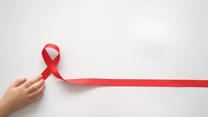AID red ribbon in child hand on white background, symbol of struggle against HIV, AIDS and cancer. Concept of helping those in need. Charity, donation, donor. 4K