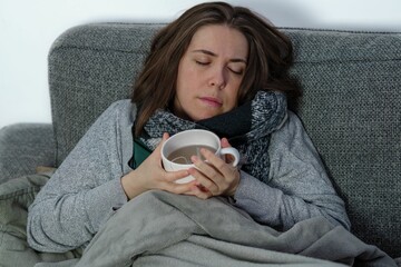 girl covered with a blanket on the couch of her house asleep while drinking a cup of tea.