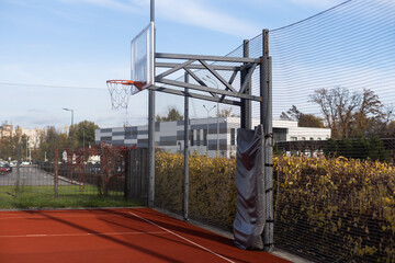 outdoor basketball in front of a blue sky. The basketball hoop or ring is orange and its pole is black.