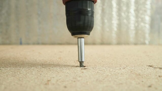 Driving a screw into a wood panel. Fastening the floor from chipboard to the logs. Close-up. Repair work.