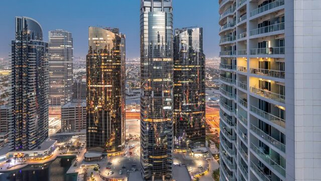 Tall residential buildings at JLT district aerial day to night transition timelapse, part of the Dubai multi commodities centre mixed-use district. Many balconies on towers