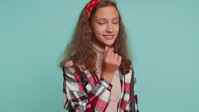 Smiling playful happy young teenager child girl kid 12 years old blinking eye, looking at camera with toothy smile, winking and flirting expressing optimism. Preteen children on studio blue background