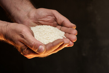 Hands holding a heap of dry rice grain on black background