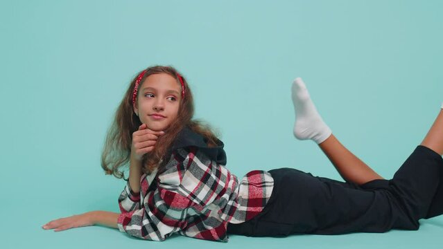 Cheerful lovely young teenager child girl kid 12 years old smiling, looking at camera. Happy preteen female children schoolgirl student isolated portrait lying on studio blue background. Childhood