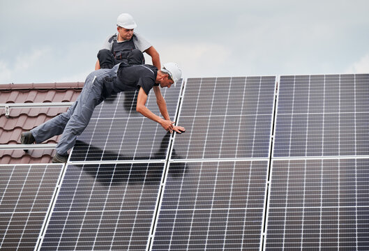 Men installers mounting photovoltaic solar moduls on roof of house. Electricians installing solar panel system outdoors, tightening with hex key. Concept of alternative and renewable energy.