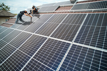 Man technician mounting photovoltaic solar moduls on roof of house. Mounter in helmet installing solar panel system outdoors. Concept of alternative and renewable energy. Aerial view. © anatoliy_gleb
