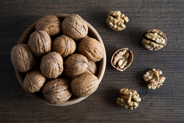Bowl of walnuts and whole walnut kernels on wooden table