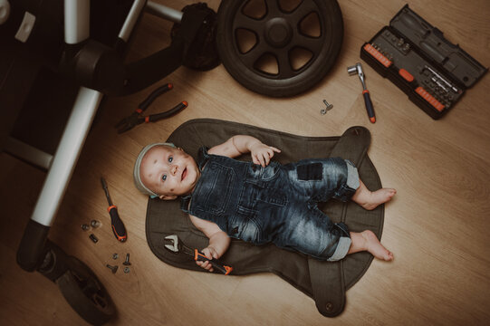 Mechanic baby boy repairing his baby stroller. Humor. Kid with tools changes the wheel. Top view.