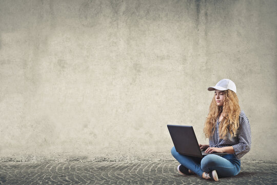 young girl sitting on the floor near a gray wall works on the computer