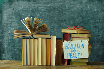 Stack of hardback books with Education brings peace slogan sign on blackboard...