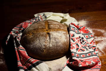 fresh baked round crunchy bread in a towel with folklore ornament - on a dark wooden background -...