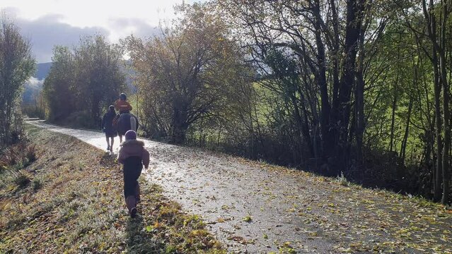 Happy family horseback riding in autumn sun - Boy with autism on top of horse while mother holding leash - little sister running into frame to catch up with mother - Idyllic handheld autumn clip