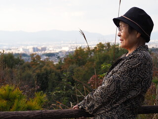 山頂の展望台から景色を眺める高齢日本人女性とススキ