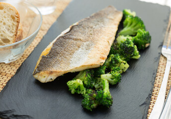 fried fillet of sea bass with garnish of broccoli on black warm stone plate