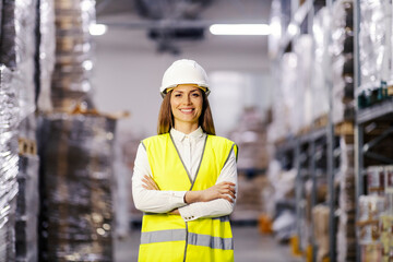 Happy female storehouse manager is standing with arms crossed and smiling at the camera.