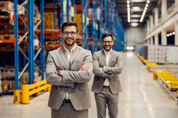 Two successful managers are standing in warehouse with arms crossed.