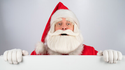 Santa Claus peeks out from behind an ad on a white background. Merry Christmas.