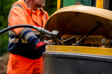 Builder in safety gloves filling excavator with diesel fuel on building site