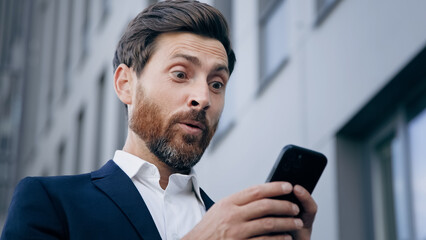 Close-up young surprised man looks at phone screen receiving notification reading good news...