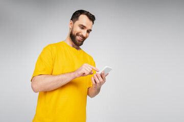 low angle view of brunette bearded man pointing at mobile phone isolated on grey.
