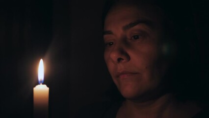 A Caucasian woman prays while standing in front of a burning candle. The girl gazes at the candle in front of her.