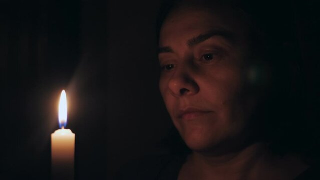 A Caucasian woman prays while standing in front of a burning candle. The girl gazes at the candle in front of her.
