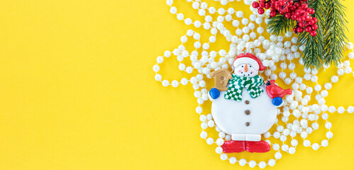 banner with Snowman with a branch of Christmas tree and Christmas beads on yellow background. Christmas background. New Year concept. Top view