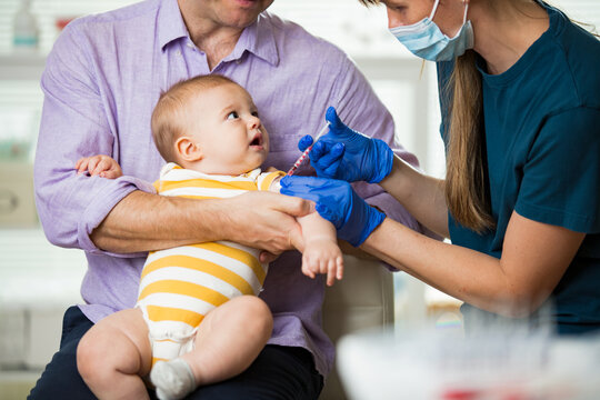 Female nurse with surgical mask and in gloves giving vaccine injection to a baby in clinic. Infant children vaccination. 