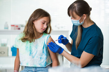 Female nurse with surgical mask and in gloves giving vaccine injection to a teenager in clinic. Children vaccination. 