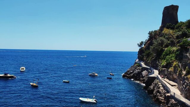 Boats floating in the Amalfi coast sea. Looking from the port to the open sea. Rowboat, fishing boats and yachts on a sea. Blue transparent water with cliffy shore. Rocky cliffs, floating boats. 
