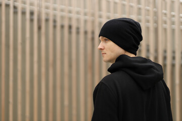 Young man in a black beanie hat and hoodie on a wooden background.