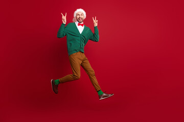 Fototapeta na wymiar Full length photo of carefree excited guy jumping hands fingers demonstrate v-sign isolated on red color background