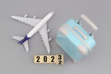 Airplane with travel suitcase and flipping numbers 2022 and 2023 on gray background. Tourism in new 2023 year.	
