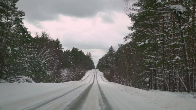 Driving with caution on a slippery road covered with snow in the forest. Car driving on empty path in winter.
