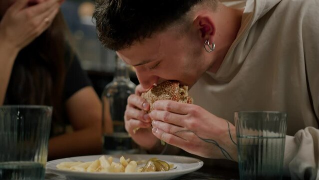 close-up - a man guy eats a burger and french fries in the company of friends