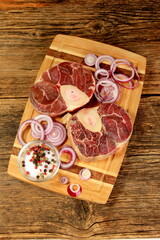 Raw fresh cross cut veal shank, red onion and pepper on kitchen board. Osso Buco on wooden cutting board