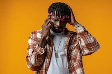 Young african man talking on smartphone stressed with hand on head on yellow background