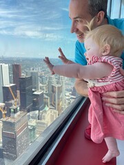 Bébé devant une baie vitrée avec vue sur la ville avec son papa