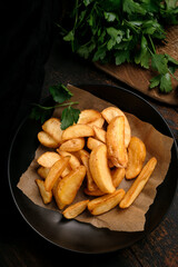 Fried potatoes in large pieces in a black plate on a rustic wooden background, top view