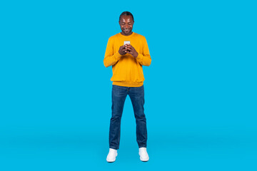 Fototapeta na wymiar Happy african american man using cell phone isolated on blue