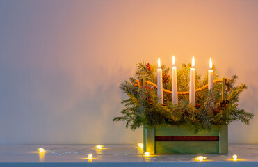 advent decoration with fir branches and four burning candles in wooden basket on white background