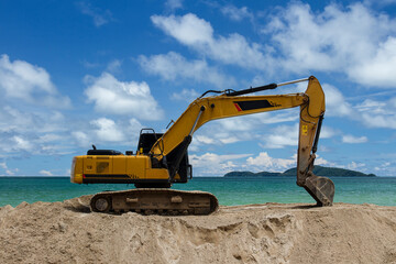 Fototapeta na wymiar Excavator is scooping up sand on the beach with sky, sea and island background..Excavator is digging sand on the beach.