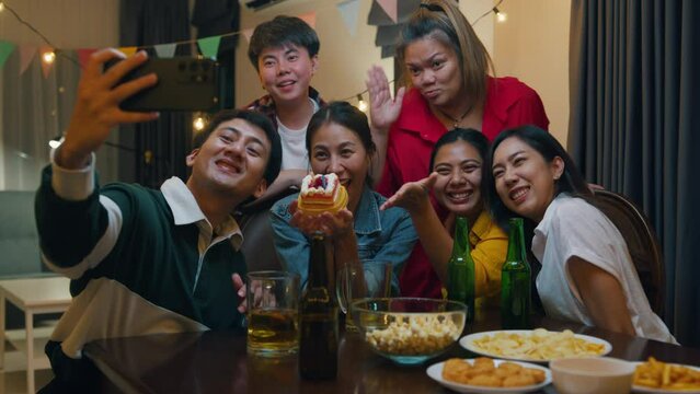 Group of young adult Asia friend with birthday cake look at camera shooting video photo on mobile app fun hangout party in night life indoor home. Happy hour time millennial generation inside house.