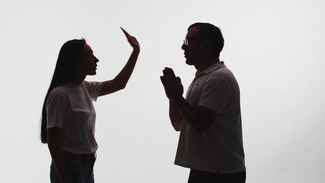 Young woman with emotional gestures rejecting the apology of a man in glasses on a white background. Couple swearing with each other during emotional quarrel