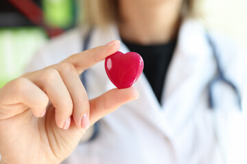 Female cardiologist with stethoscope holding red heart in hand.