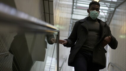 Black man wearing covid mask descending metro subway stairs touching handrail