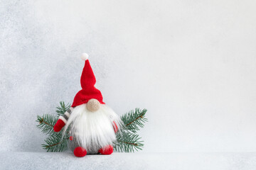 Christmas gnome in red cap with fir branch holiday invitation card on light winter background....
