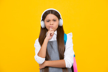 School girl, teenager student in headphones on yellow isolated studio background. Music school concept. Thinking face, thoughtful emotions of teenager girl.