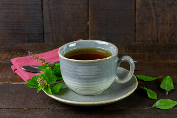 Tulsi or holy basil tea in gray cup with fresh tulsi leaf on wooden background. Ayurvedic medicine in India.