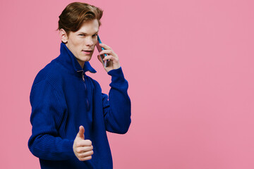 portrait of a funny guy with red hair showing a thumbs up during a telephone conversation. Monochromatic pink backdrop studio photography with advertising space